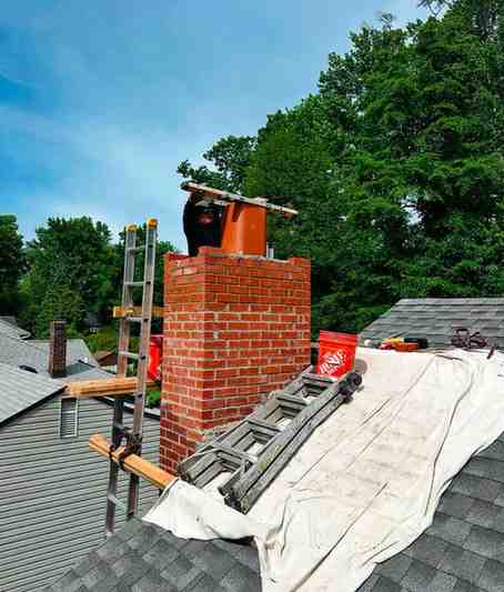 Chimney rebuild in progress with tarps and scaffolding on a shingled roof