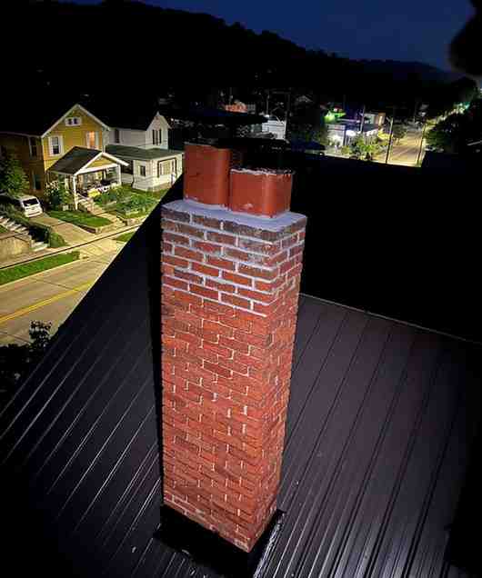 Freshly rebuilt brick chimney on a metal roof at dusk